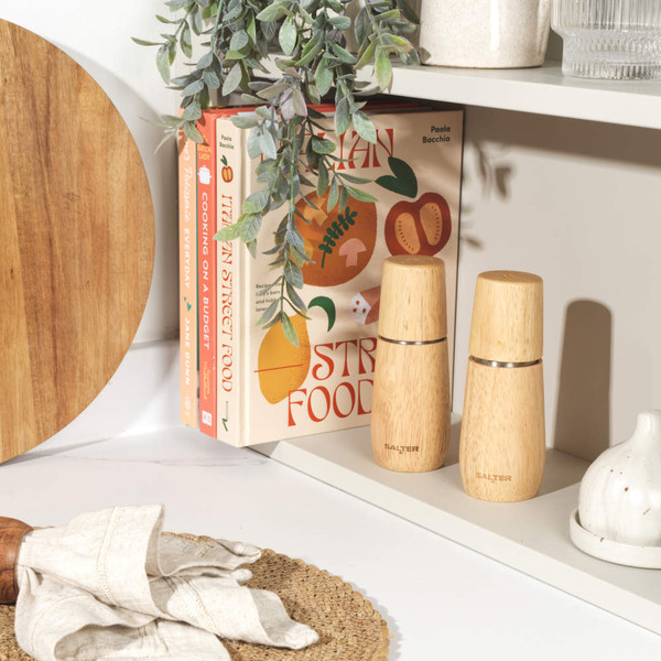 Natural wood salt grinder and bowl of sea salt on kitchen counter