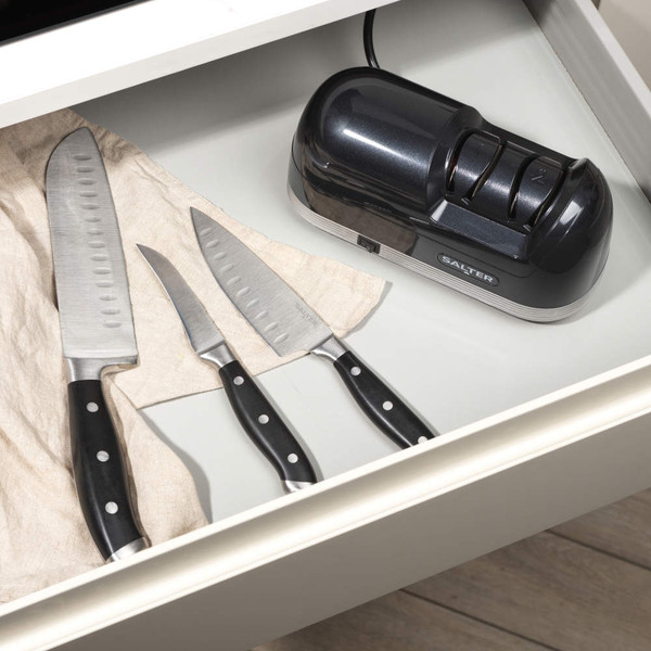 Electric knife sharpener and black-handled kitchen knife on white countertop