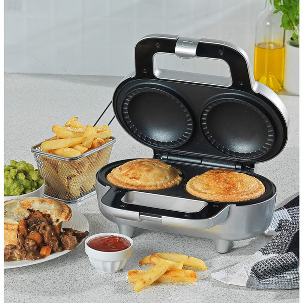 Silver pie maker with two cooked pies, steak pie meal and chips on a kitchen counter