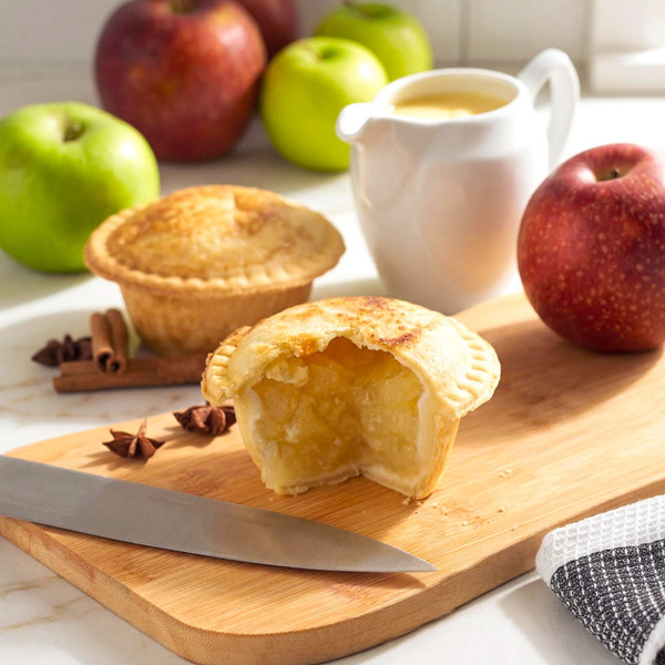Apple pie with filling on wooden board, cut open to show inside, knife and apples nearby