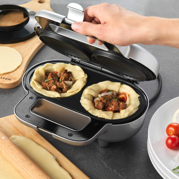 Silver pie maker with two steak filling pies, shown open and ready to bake.