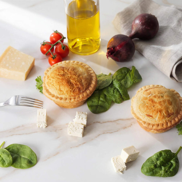 Two golden pies with spinach and cheese on marble, assorted fresh ingredients nearby