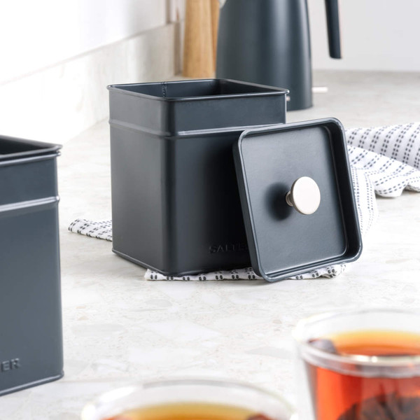 Set of three square grey metal storage canisters on kitchen counter, one with tea bags visible
