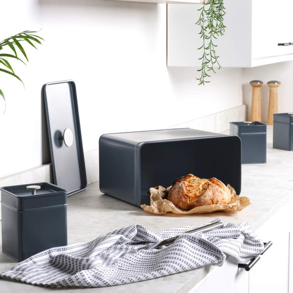 Set of black metal kitchen storage canisters on worktop with bread and butter in foreground