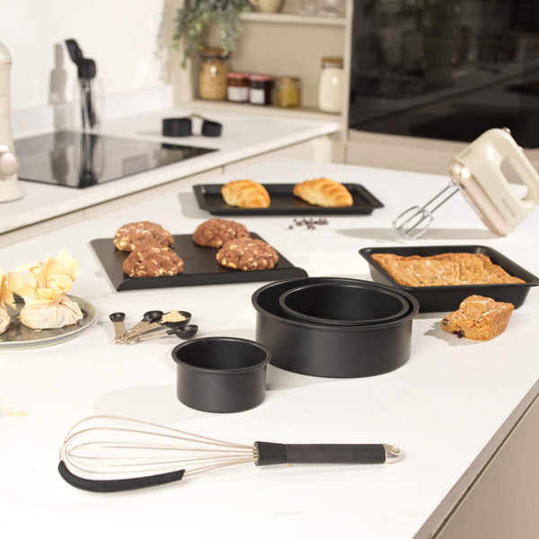 Non-stick black baking tray set on kitchen counter with cookies, cake, and croissants