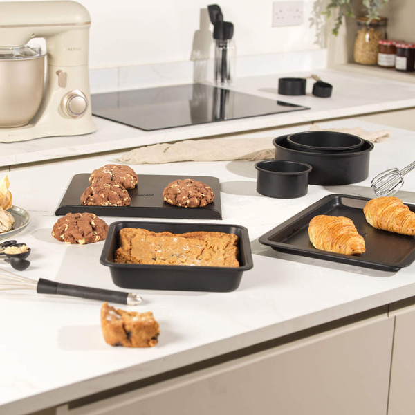Non-stick black baking tray set on kitchen counter with cookies, cake, and croissants