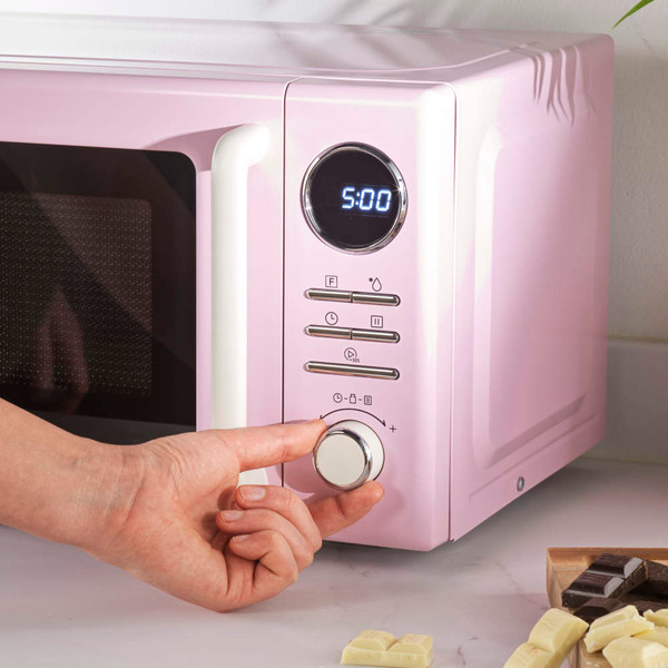 Pink microwave on kitchen counter with wooden utensils and glass bowl of chocolate