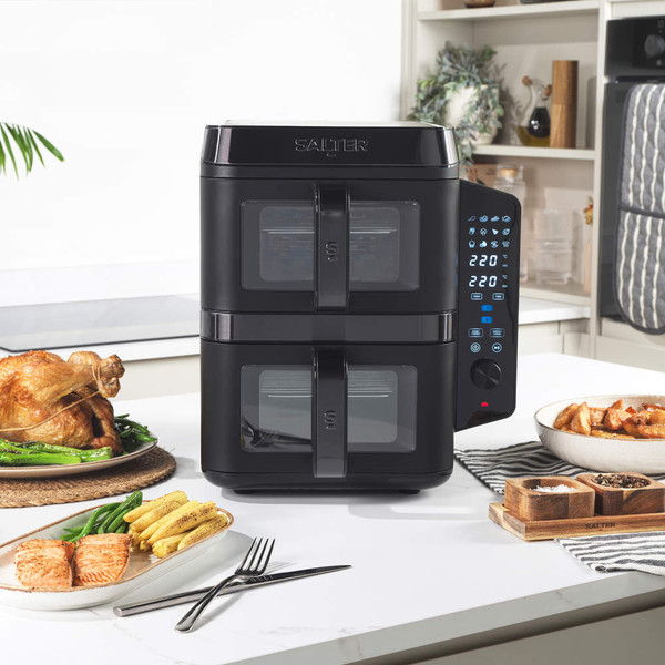 Black double drawer air fryer on kitchen counter with control panel, food served beside.