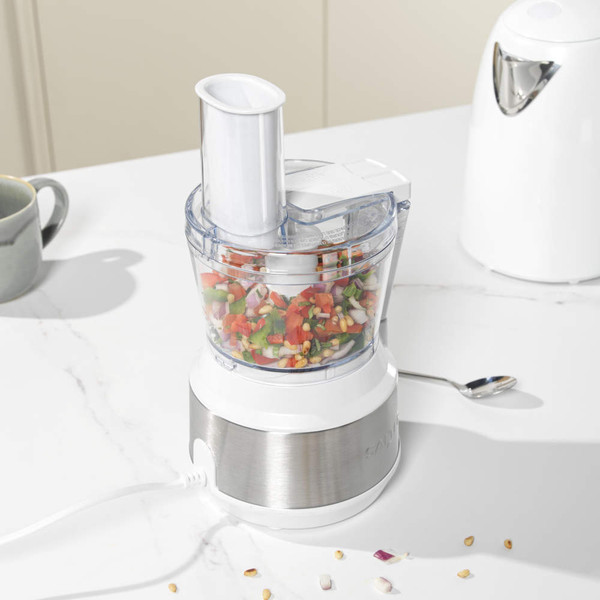 White food processor with clear bowl chopping mixed vegetables on a kitchen counter