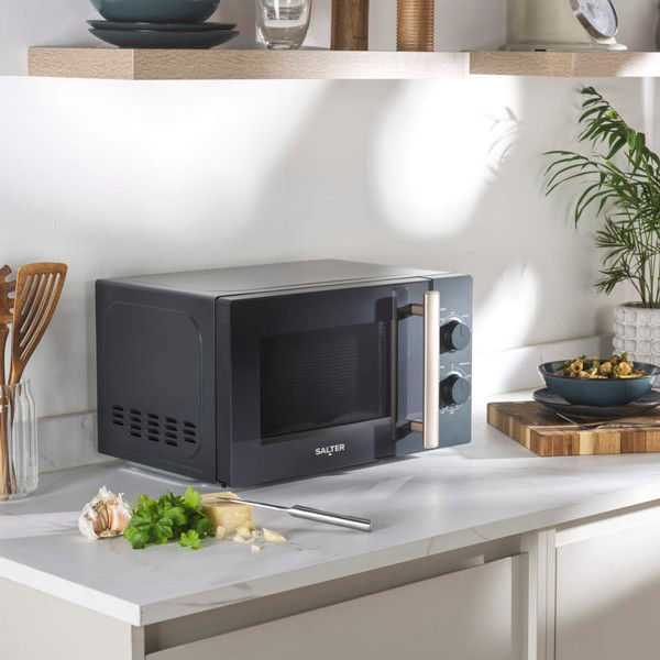Grey microwave oven with mechanical dials shown heating food, door open