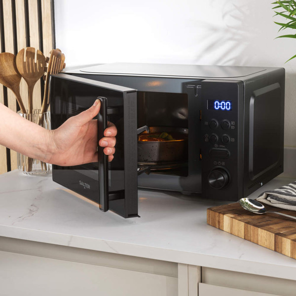 Black digital microwave oven with blue LED display, hand turning control knob, on kitchen counter