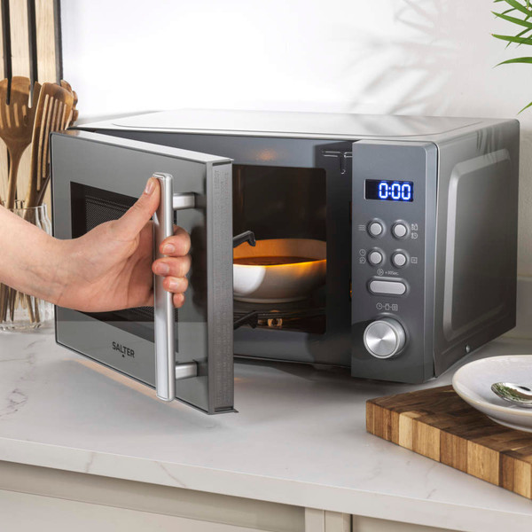 Silver microwave on kitchen counter, door open, hand reaching in to remove bowl