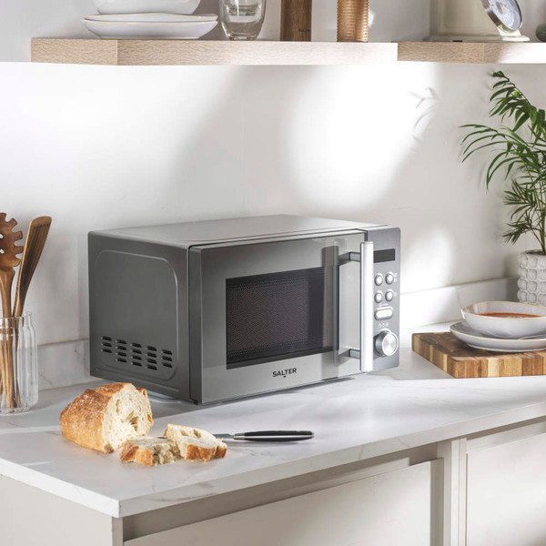 Silver microwave oven on kitchen counter, shown with bread and crockery, UK home setting