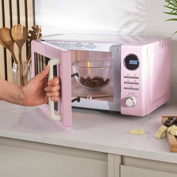 Pink microwave oven with digital display, shown on a kitchen counter with cooked food