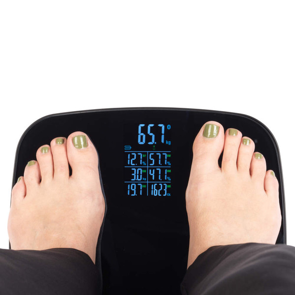 Person standing on black digital bathroom scale displaying weight and body stats