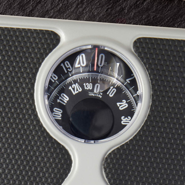 Mechanical bathroom scale with black textured platform, showing close-up of dial.