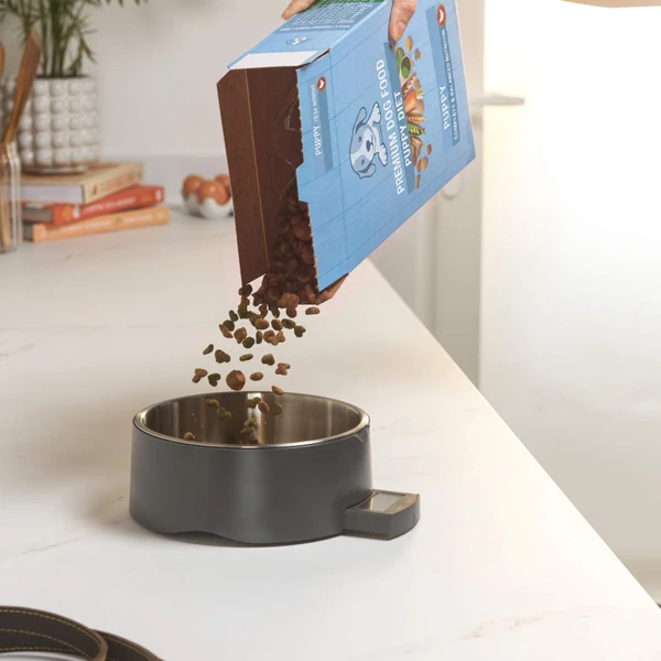 Pouring dry puppy food into a grey dog bowl on a kitchen counter