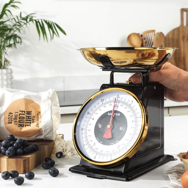 Black mechanical kitchen scale with gold bowl, shown side-on