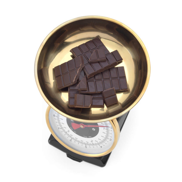 Broken dark chocolate pieces on a gold metal kitchen scale bowl