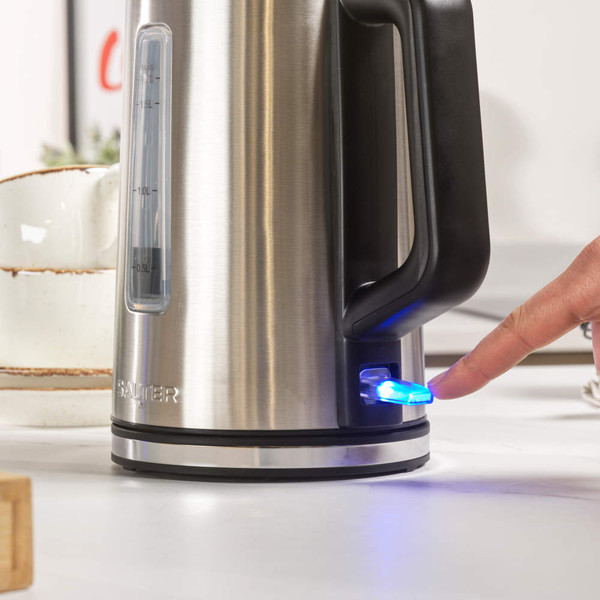 Stainless steel electric kettle with black handle, being switched on by a person's finger