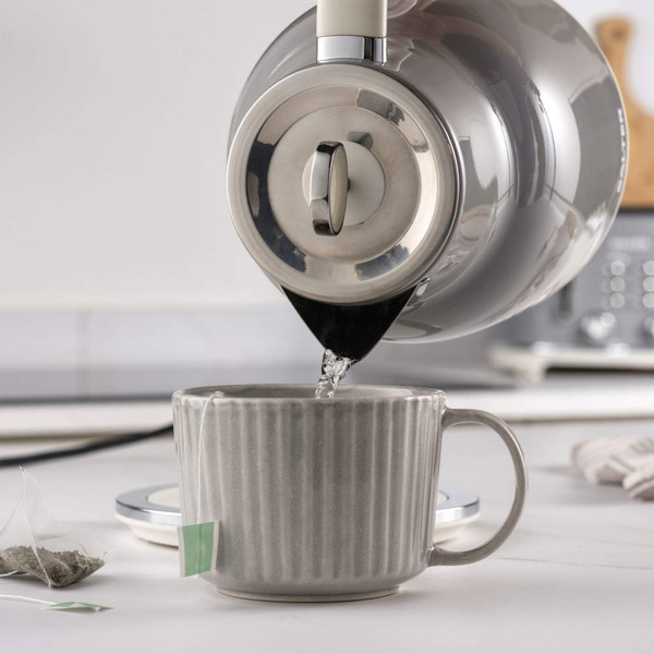 Kettle pouring hot water into grey mug with tea bag on kitchen counter