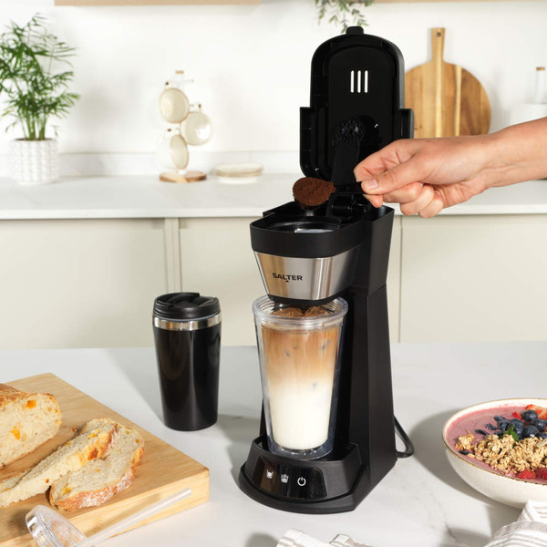 Salter stainless steel electric grinder on wooden countertop, surrounded by herbs and spices