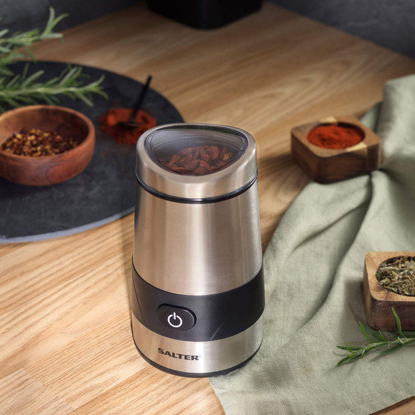 Stainless steel coffee grinder with lid open and whole coffee beans inside, on wooden surface