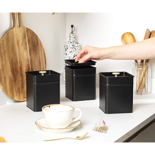 Set of three matte black kitchen storage tins, one with lid open on worktop
