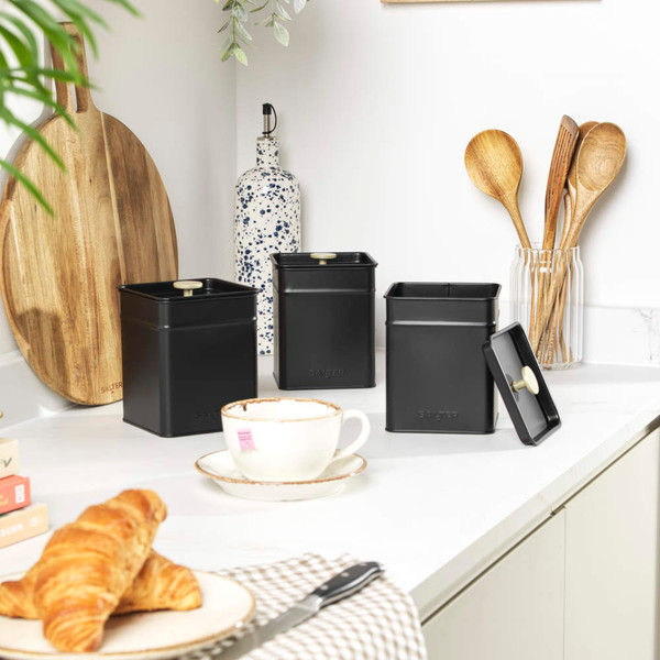 Set of three black kitchen storage canisters with lids on a white worktop