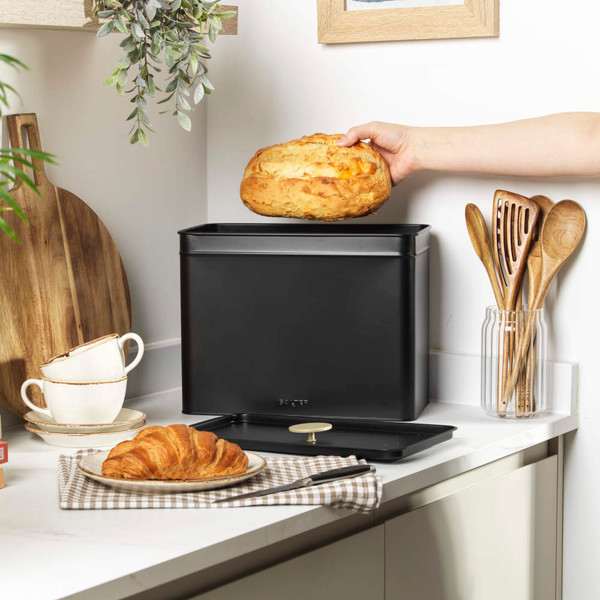Black metal bread bin with lid open, loaf inside, on modern kitchen counter