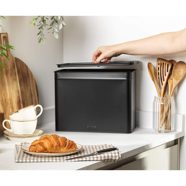 Black metal bread bin on kitchen counter, lid being lifted by hand