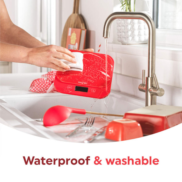 Red kitchen scale being wiped under running tap, showing waterproof cleaning feature