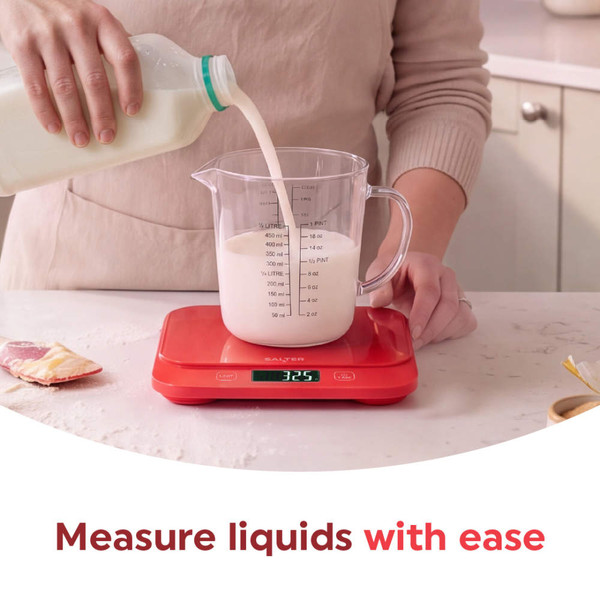 Red digital kitchen scale with strawberries on top, shown on a kitchen countertop