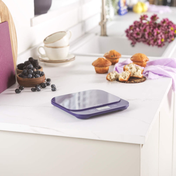 Blue digital kitchen scale on white worktop, shown with muffins and berries.