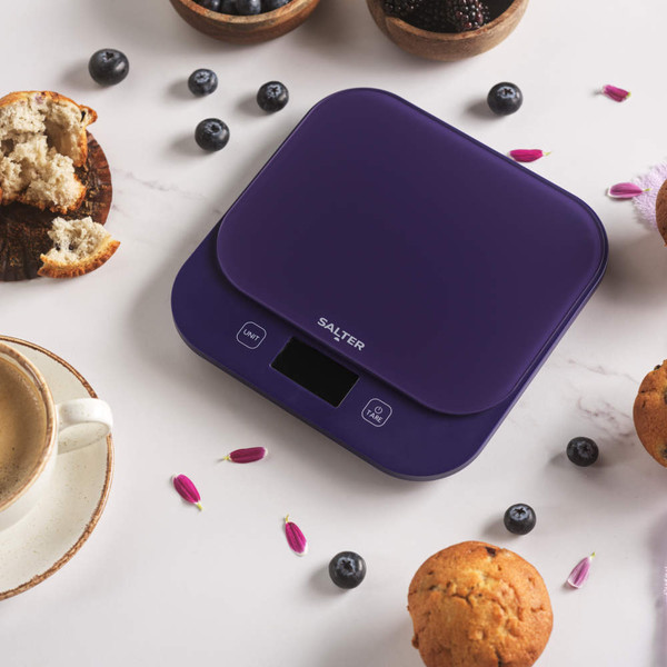 Digital kitchen scale in dark blue with display, surrounded by muffins and blueberries