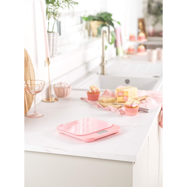 Glass mixing bowl with flour, butter and egg on pink digital kitchen scales, baking ingredients beside