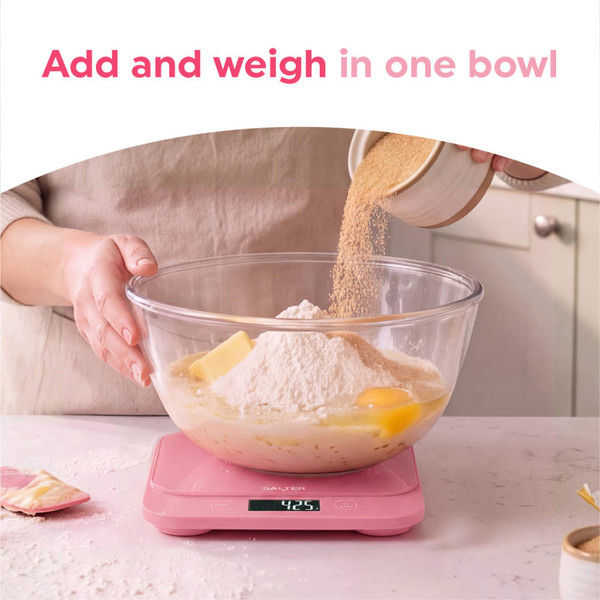 Person cleaning pink digital kitchen scale under running tap in modern sink