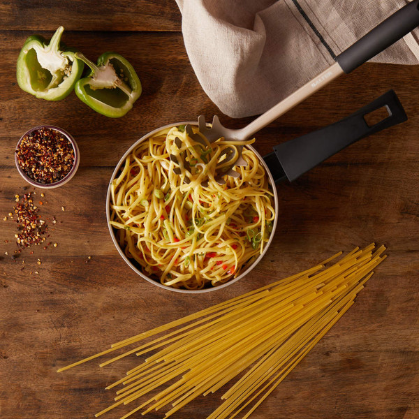 Cooked spaghetti with peppers in saucepan, utensil and raw pasta on wooden table.