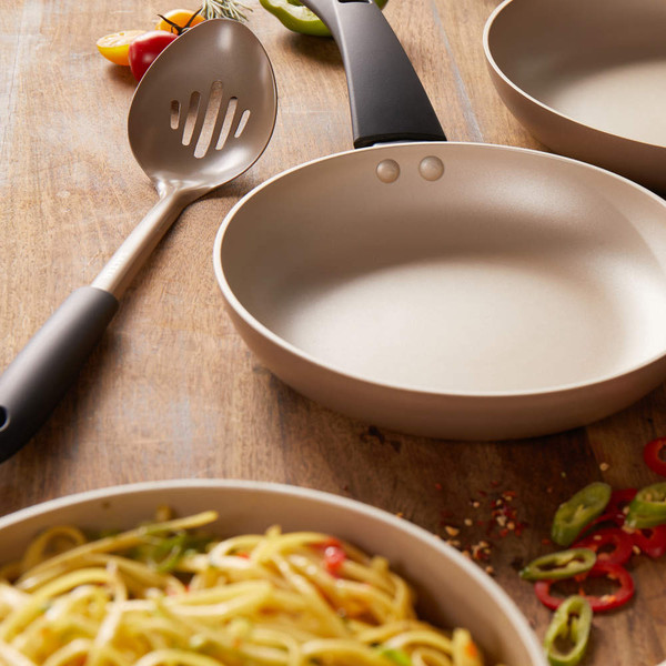 Non-stick beige frying pan with black handle, shown with slotted spoon and cooked pasta.