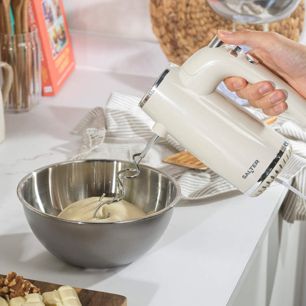 Cream hand mixer in use, mixing dough in a metal bowl on a kitchen counter