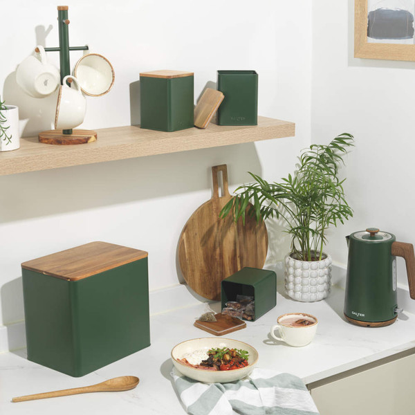 Set of three green metal kitchen storage canisters with wooden lids, one filled with sugar cubes.