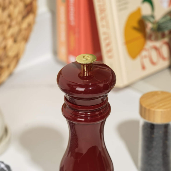 Glossy red pepper mill with brass top, shown on a kitchen counter