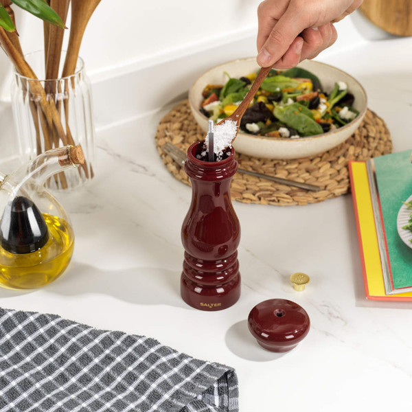 Red glossy wooden pepper mill showing ceramic grinder, angled side view