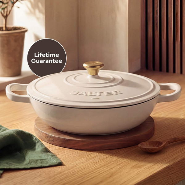 Cream cast iron casserole dish with lid and gold knob, shown on rustic kitchen table