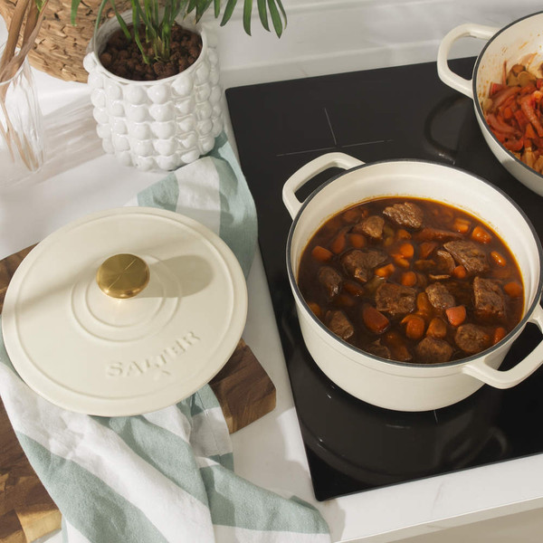 Cream cast iron casserole dish with lid, filled with beef stew, on kitchen hob