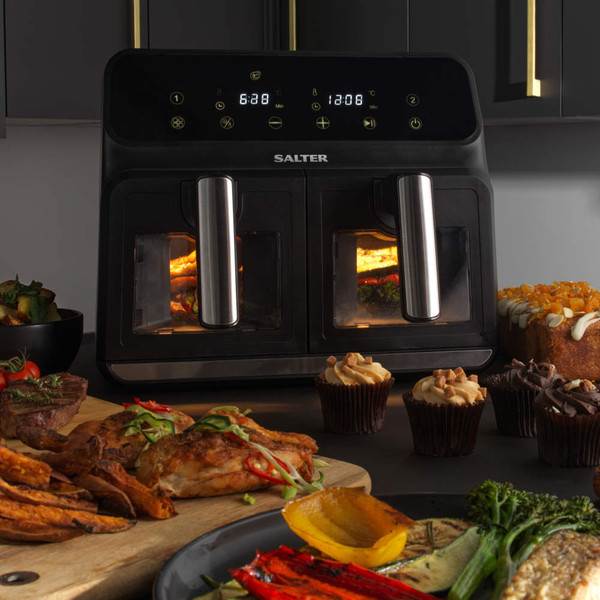 Black dual basket air fryer on kitchen counter with cooked chicken, vegetables and cupcakes