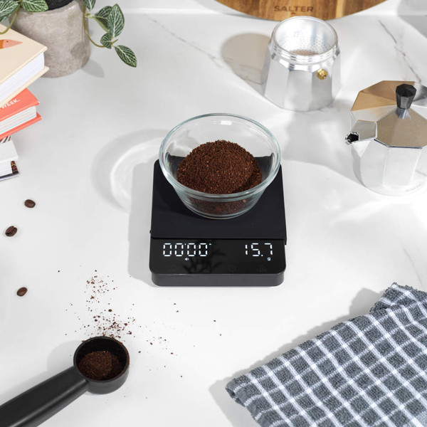 Black digital coffee scale with glass jug and filter, top view, on white background