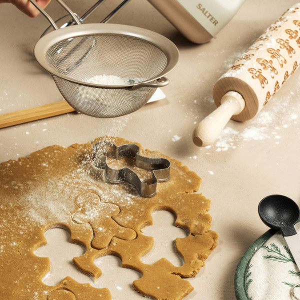Gingerbread cookie dough with gingerbread man cutter, rolling pin and flour being sprinkled