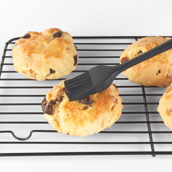 Pastry brush glazing golden raisin scones on cooling rack