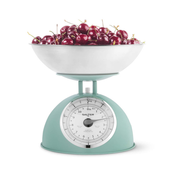 Sage green kitchen scale with metal bowl, filled with fresh cherries.